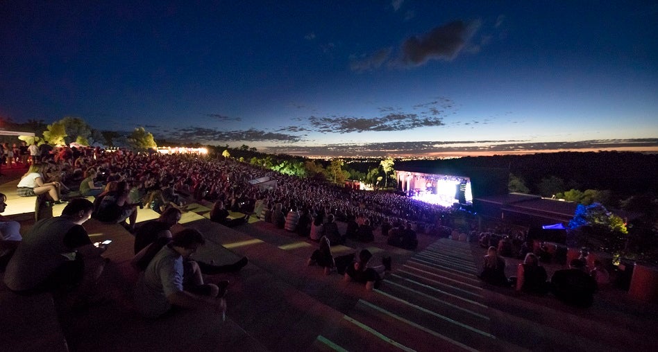 Photo of a large stage in the middle of a forrest surrounded by people enjoying music