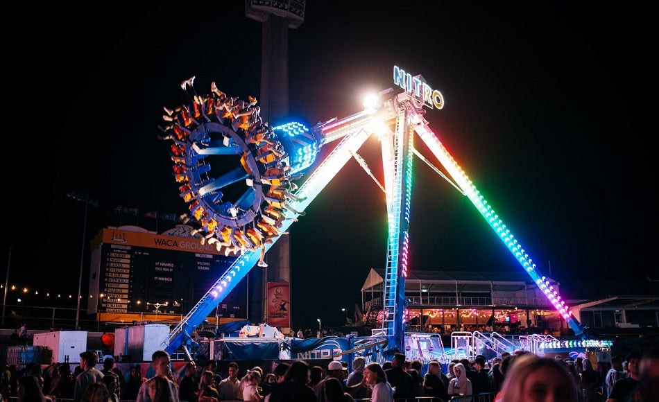 Photo of people on a lit up amusement ride with people walking past